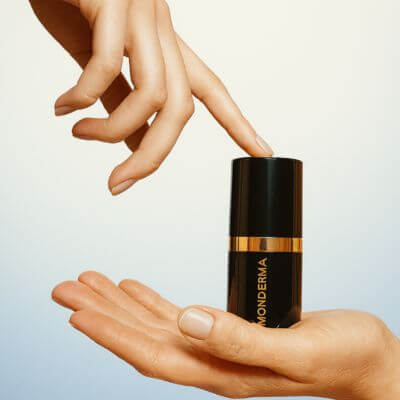 Two hands holding a Monderma custom formula against a soft gradient background class=